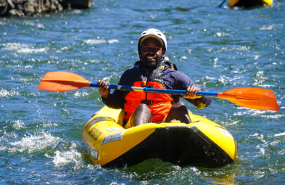 Person of color in an inflatable kayak smiles for the camera while floating down the Rogue River