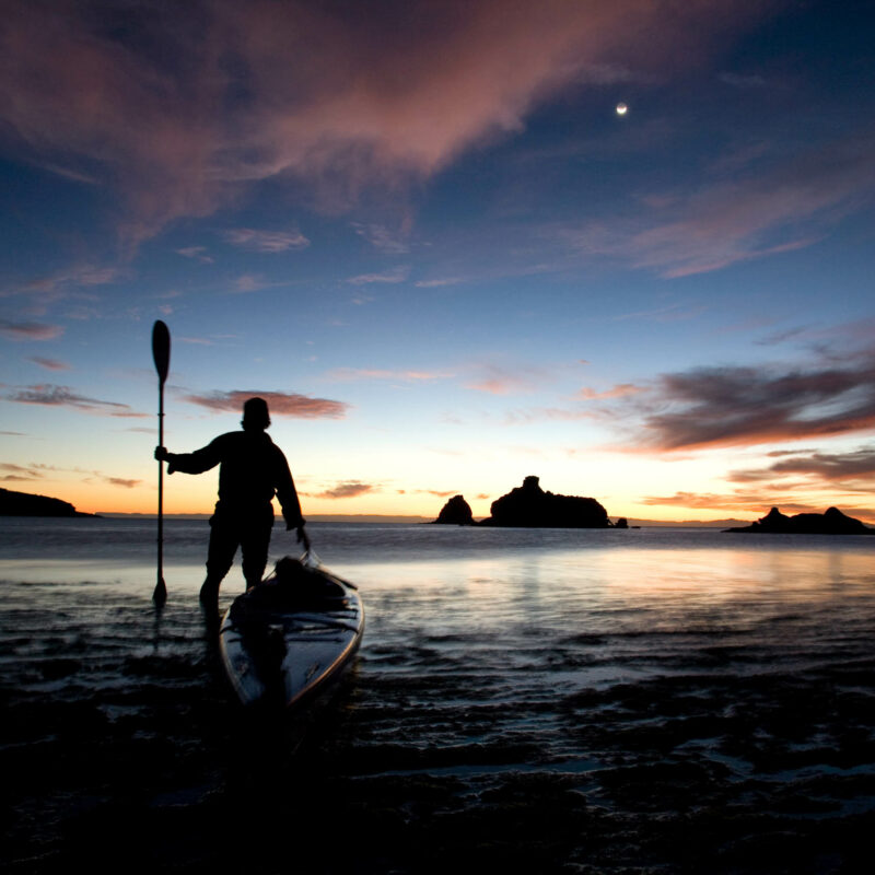 Person next to their sea kayak at sunset.