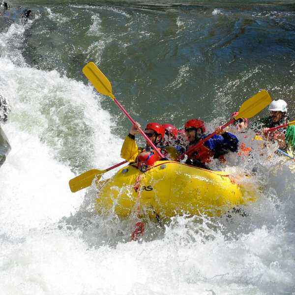 A yellow raft full of paddlers crashes up through a big rapid on the American River.