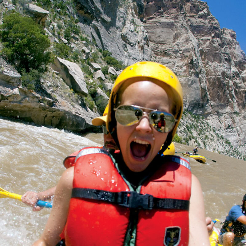 A kid exhinits joy and excitement as they sit on a paddle raft going through white water.