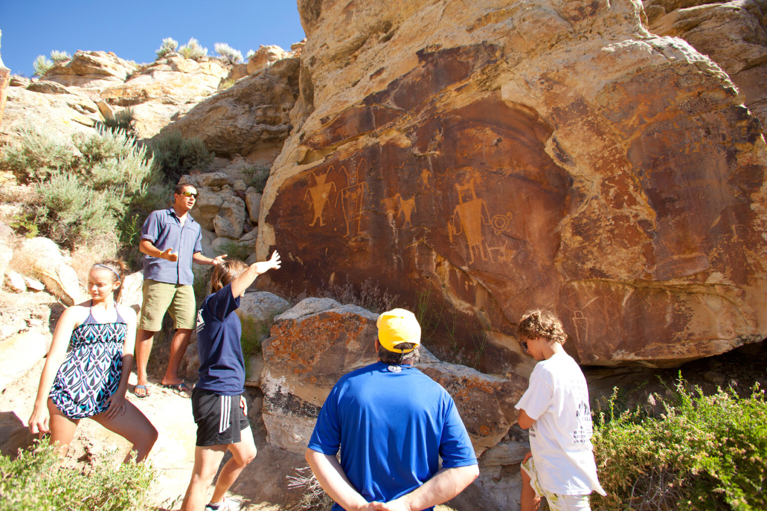 A guide stands in front of a wall of petroglyphs and gives an interpretive talk while guests listen.