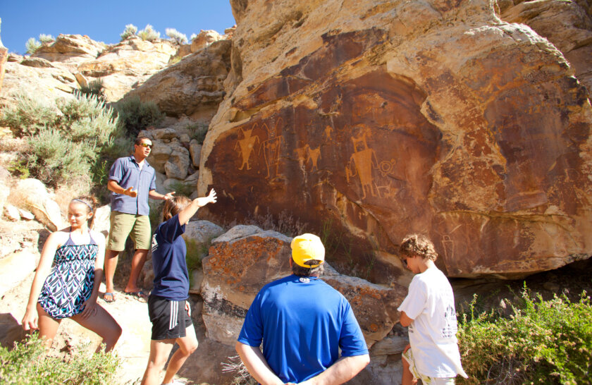 A guide stands in front of a wall of petroglyphs and gives an interpretive talk while guests listen.