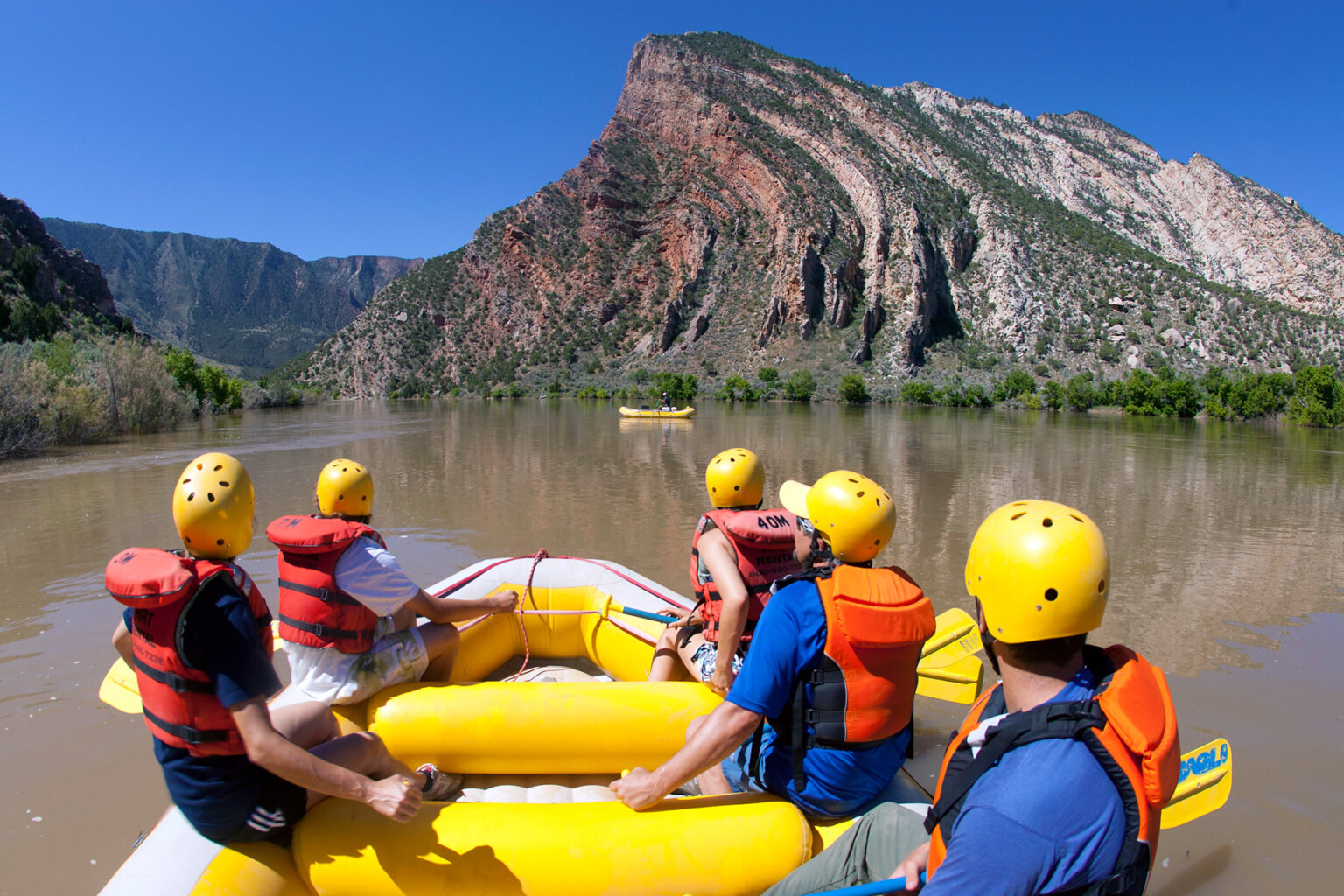 A group of people in a raft holding paddles take a moment to admire the view downstream on the Green River during a section of flat water.