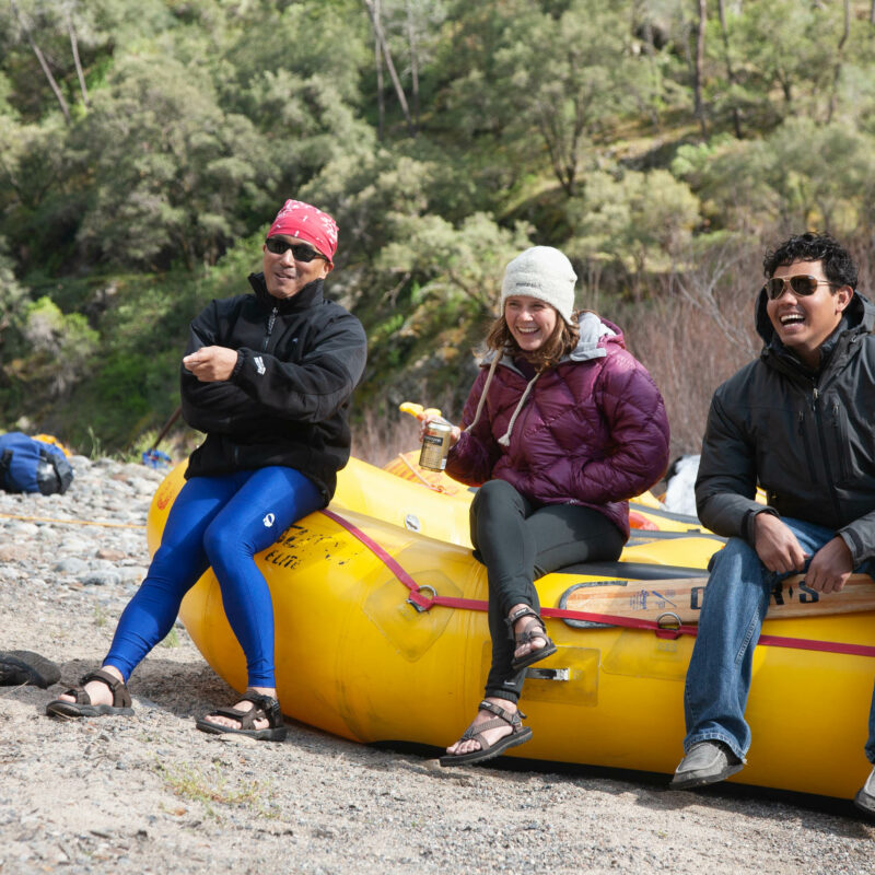 Three people sitting on the edge of the rafter laughing together.