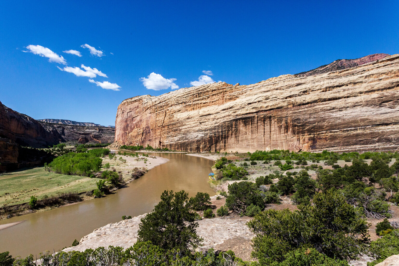Vast landscape view of the Yampa River with boats tied up at the shoreline downriver in the distance.