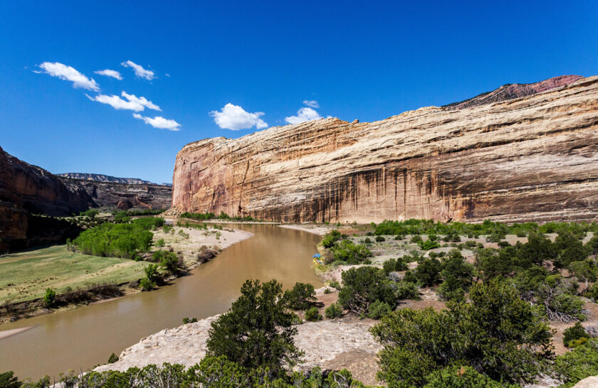 Vast landscape view of the Yampa River with boats tied up at the shoreline downriver in the distance.