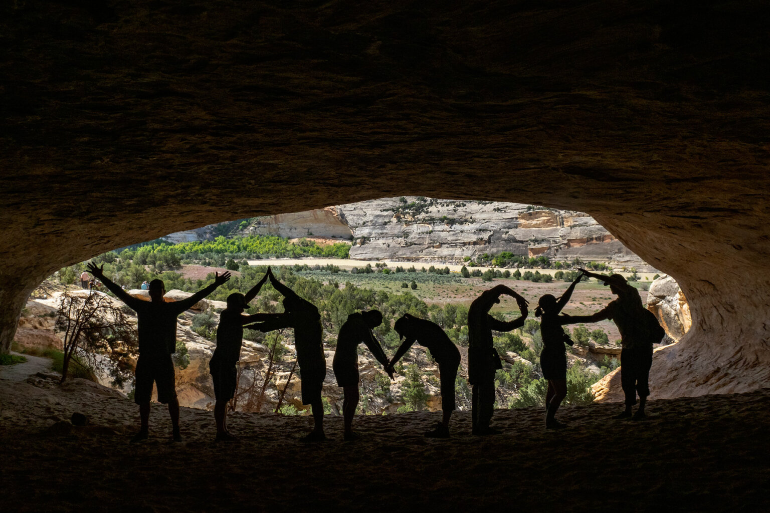 Silhouette of people in a cave with a sunny desert landscape behind them spelling out Yampa with their bodies.