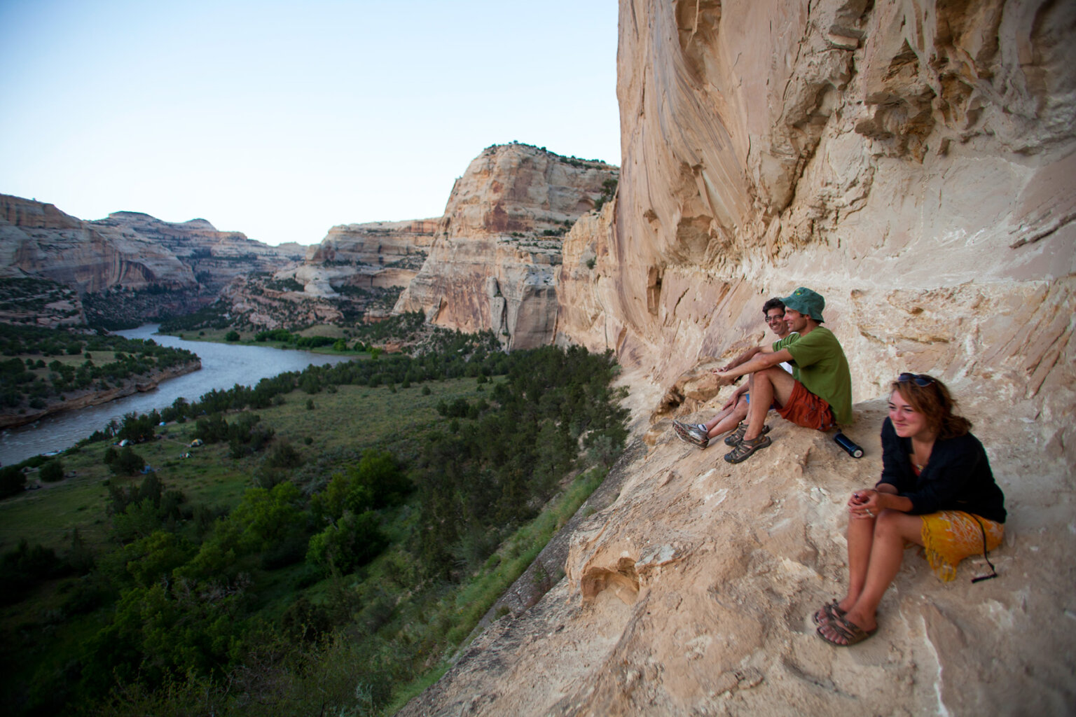 Three people sit on a rocky outcrop high above the Yampa River and rest after hiking.