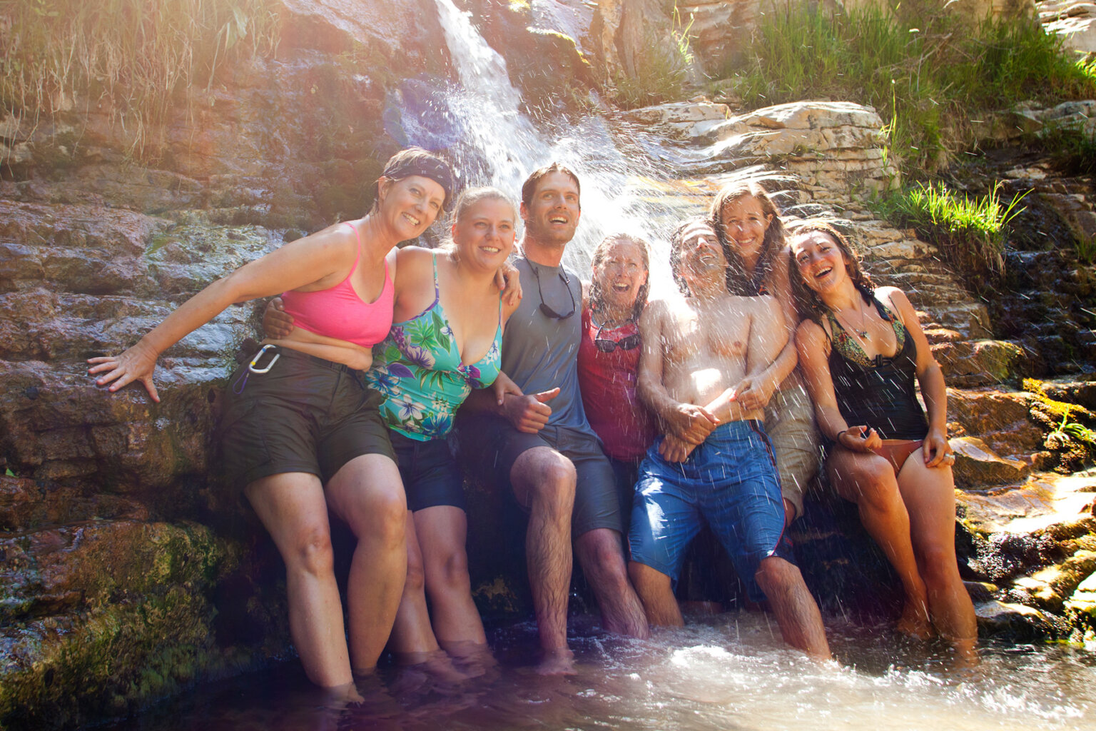 A happy smiling group pose under the spray of a small waterfall on an OARS Yampa River trip.