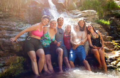 A happy smiling group pose under the spray of a small waterfall on an OARS Yampa River trip.