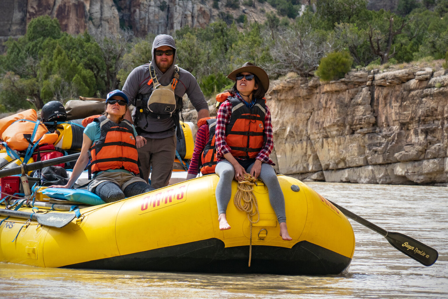 Two guests sit at the front of a yellow raft and look up at the scenery while their guide rows them downstream on the Yampa River.