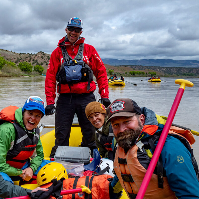 Guests and a guide smile at the camera while sitting on a yellow paddle raft on the Yampa River.