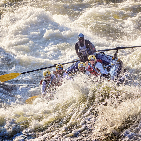 Guests paddle with a guide assisting on oars through big whitewater on the Zambezi River.